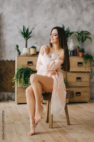 Young lady woman in pink negligee standing by the chest of drawers with flowers
