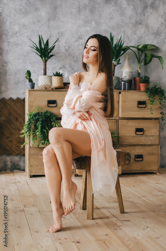 Young lady woman in pink negligee standing by the chest of drawers with flowers