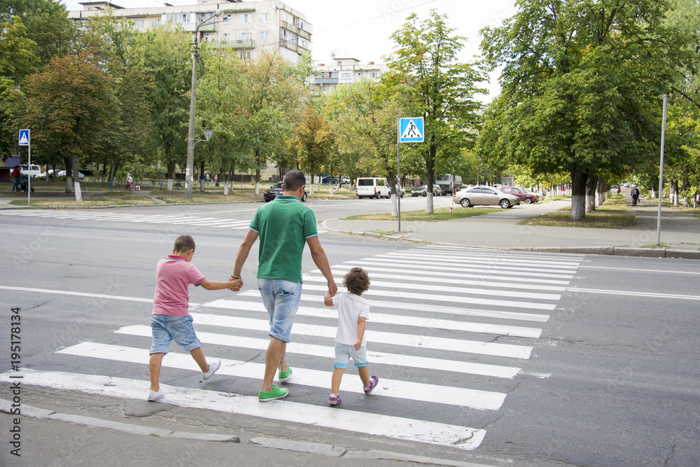 In the summer on the street at the pedestrian crossing father and son and daughter cross the road. Dad keeps the children by the hands. Stock 写真 | Adobe Stock