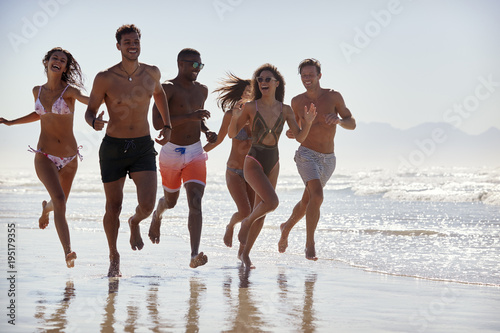 Group Of Friends Run Through Waves Together On Beach Vacation