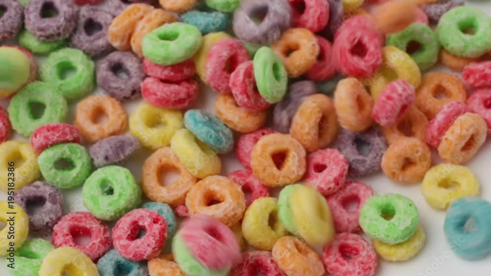 Very close video of pouring generic dry sugar coated fruity flavored breakfast cereal into a large white bowl.