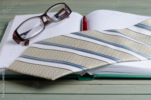 Open notebook, fountain pen, striped tie, glasses. Wooden background. photo