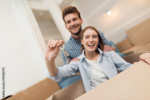 Young couple having fun while moving to new apartment. Moving newlyweds. Girl is sitting in a box. © VadimGuzhva