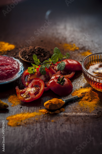 Close up of tomato,with its puree,honey,turmeric, powder of sandal wood,and turmeric powder on wooden surface in dark Gothic colors for better and healthy white skin.