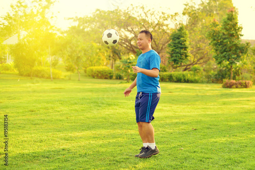 Asian man playing football alone in garden 