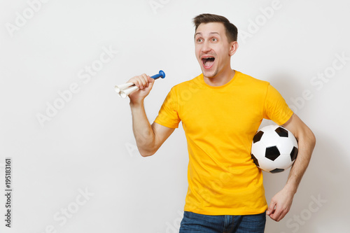 Inspired young fun cheerful European man, fan or player in yellow uniform hold soccer ball, pipe, cheer favorite football team isolated on white background. Sport, play football, lifestyle concept.