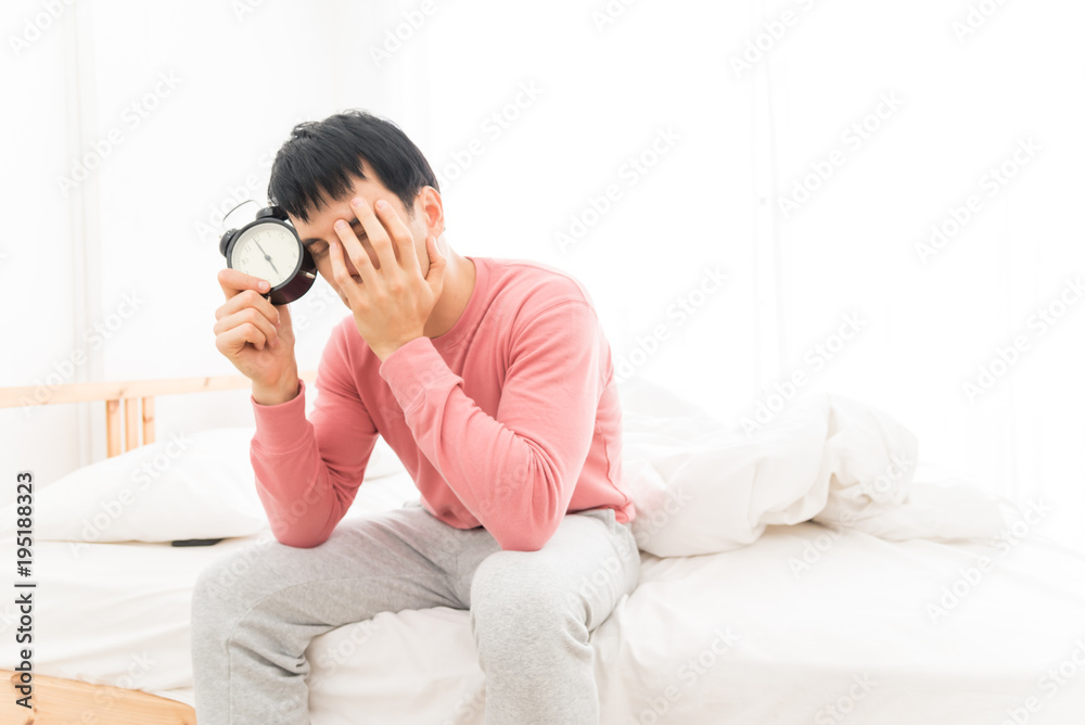 The young man was awakened by the morning alarm clock while on the bed.Shallow depth of field.unhappy from noisy sound of alarm clock and trying to turn it off. Hangover,lazy and sleepless concept. The young man was awakened by the morning alarm clock while on the bed.Shallow depth of field.unhappy from noisy sound of alarm clock and trying to turn it off. Hangover,lazy and sleepless concept.