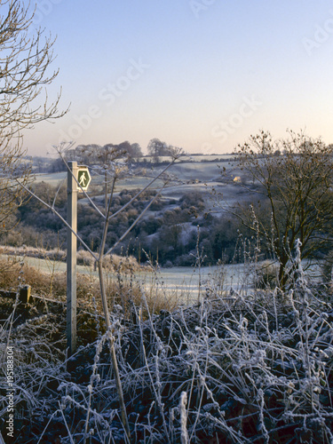 Footpath sign towards a rural valley under a heavy winter frost near Chalford, Gloucestershire, Cotswolds, UK photo