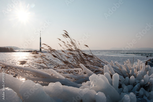 sunshine over frozen lake, light tower, port and reeds covered by ice, afternoon, Balaton, Hungary, shape of hills in background