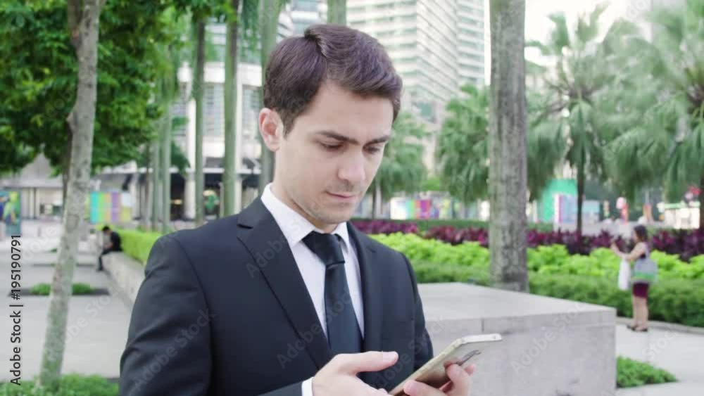 Young handsome man in business suit uses a smartphone at the street Young handsome man in business suit uses a smartphone at the street