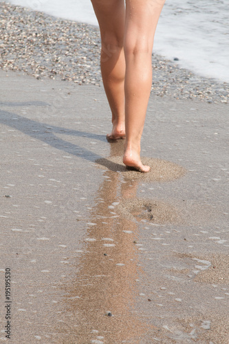 Tanned female feet, surf line, sandy beach and waves