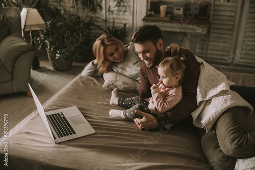 Happy family lies on bed and watching something on laptop