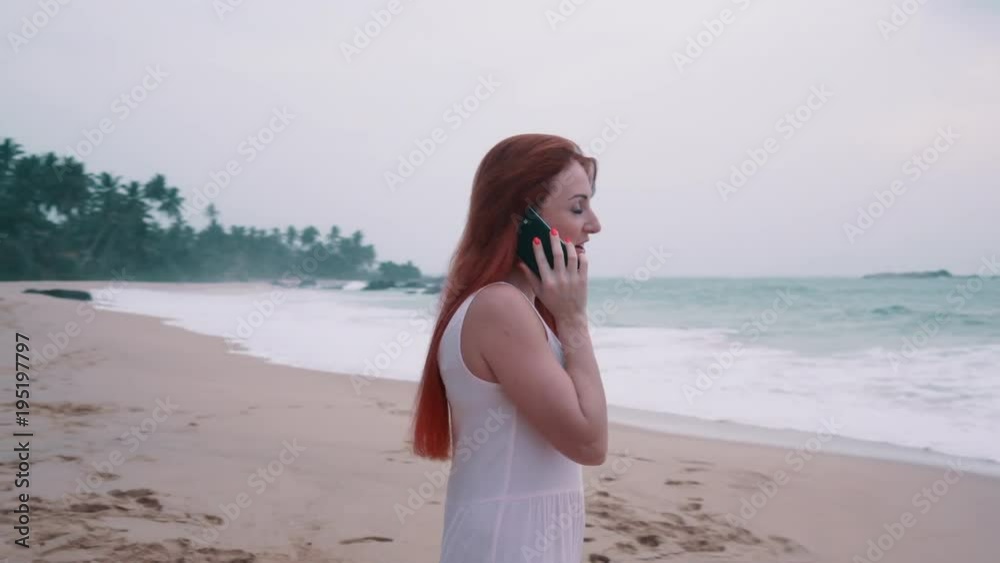 young red-haired woman talking on the phone at the ocean shore during the day young red-haired woman talking on the phone at the ocean shore during the day