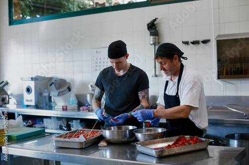 Two cooks working together with good mood and preparing strawberries for a restaurant kitchen