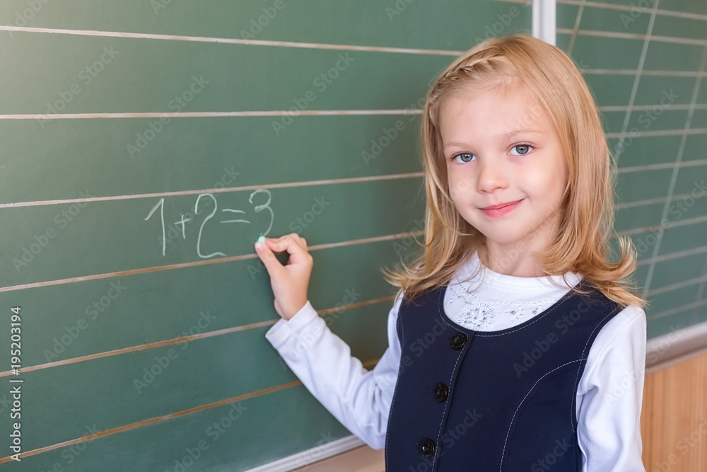 First grade pupil a girl writing on green blackboard at school lesson First grade pupil a girl writing on green blackboard at school lesson
