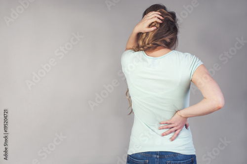 A young girl from the back with a strong headache and back pain. Convulsive spasm and headaches concept. Woman with back pain holding her aching back - body pain