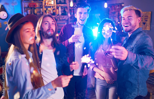 Young Group of Friends Partying In A Nightclub And Toasting Drinks. Happy Young People With Sparklers At Pub. The People Have A Great Mood And They Smile A Lot. 