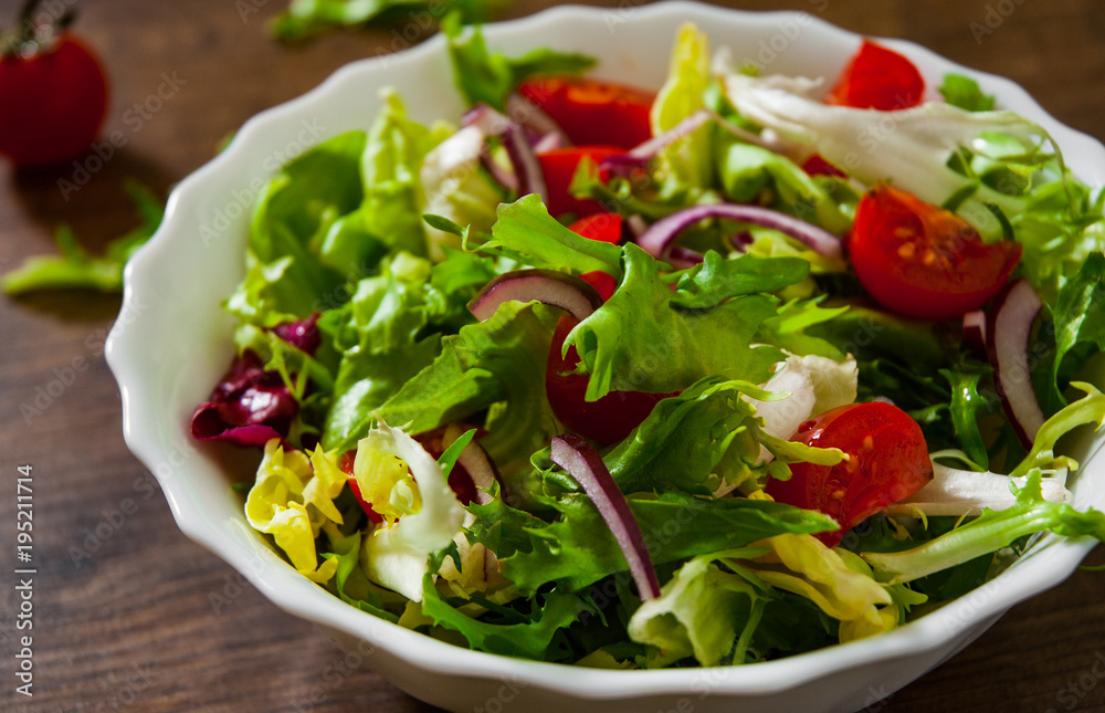 various fresh mix salad leaves with tomato in bowl on wooden background