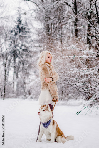 A ideal girl stands with her dog in the winter forest