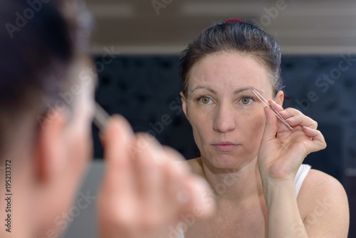 Woman plucking her eyebrows with tweezers