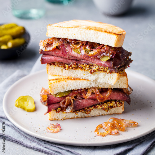 Roast beef sandwich on a plate with pickles.