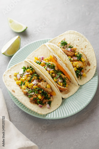 Three mexican tacos with chicken, corn, sweet pepper and parsley in the blue plate on the table.