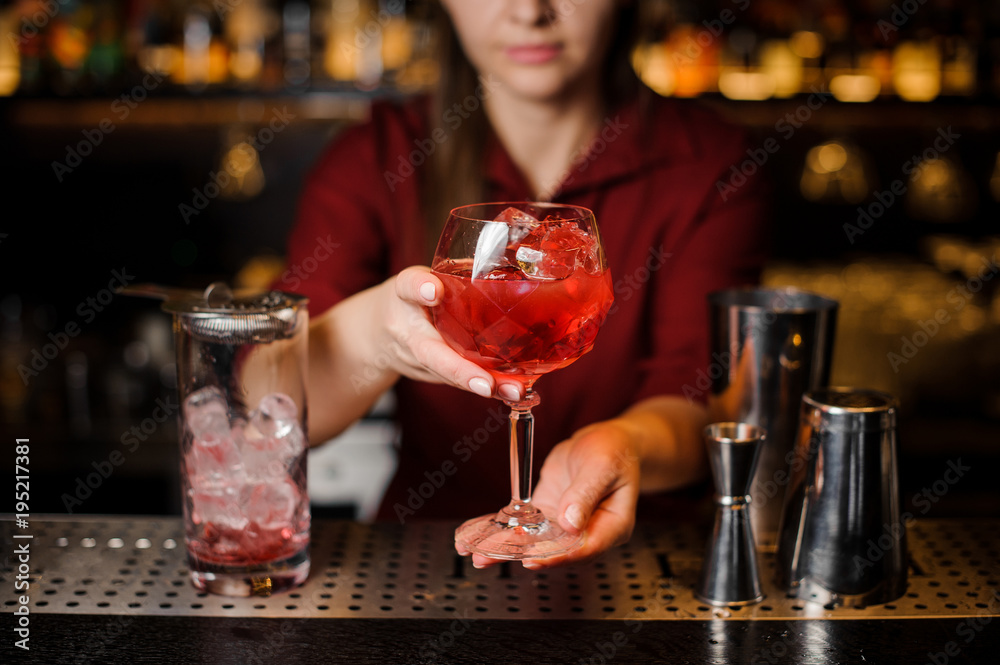 Bartender girl holding in hands a glass of red cocktail