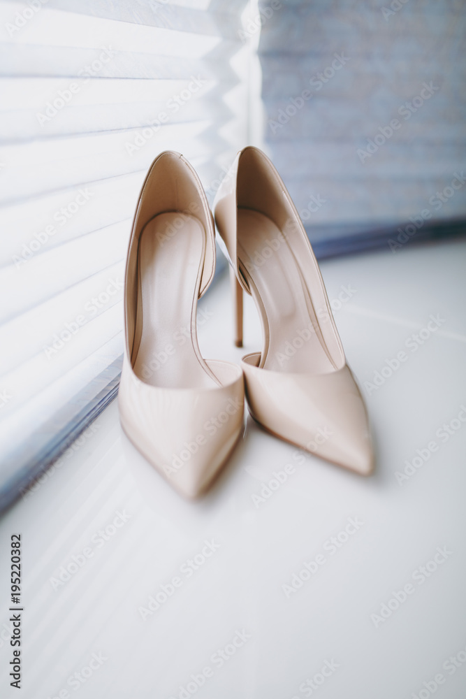 Close up Elegant light beige wedding varnish shoes with thin heels and sharp noses for the bride on a white gloss windowsill background. Wedding wear, accessories