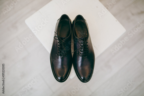 Close up Beautiful elegant wedding polished black shoes with shoelaces for the groom on a chair on background a light wooden floor. Wedding wear, accessories