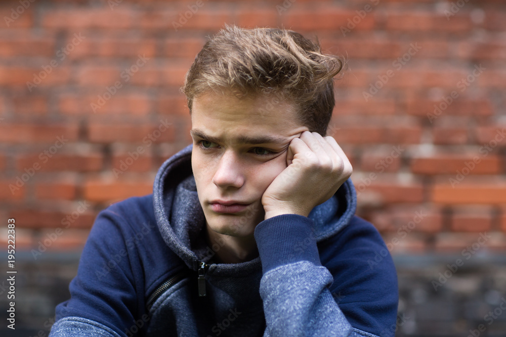 portrait of a gloomy sad teenager on a brick wall background, concept of teenage problems portrait of a gloomy sad teenager on a brick wall background, concept of teenage problems