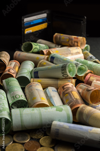Money euro coins and banknotes in rolls with a black wallet in the background
