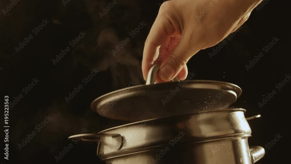 Hand opens the lid of a pot of boiling water