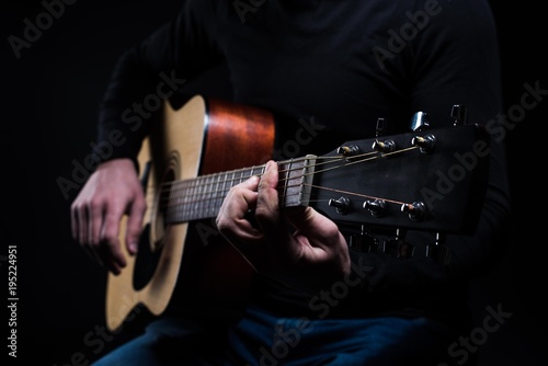 A man is playing an acoustic guitar while sitting