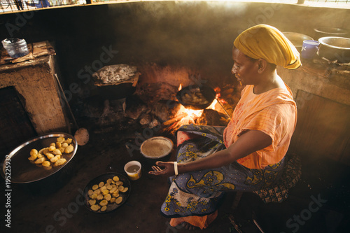 Rural African villager making bread and cooking over a fire in her kitchen photo