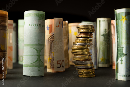 Stack of euro coins and rolls of bank notes in the background