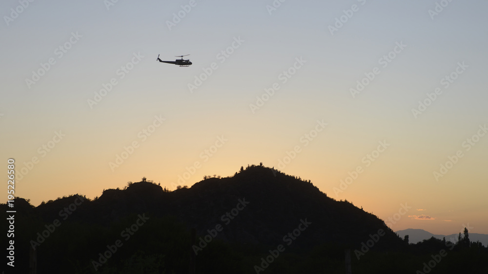 Argentinian military helicopter flying aver a range with cactusses at sunrise