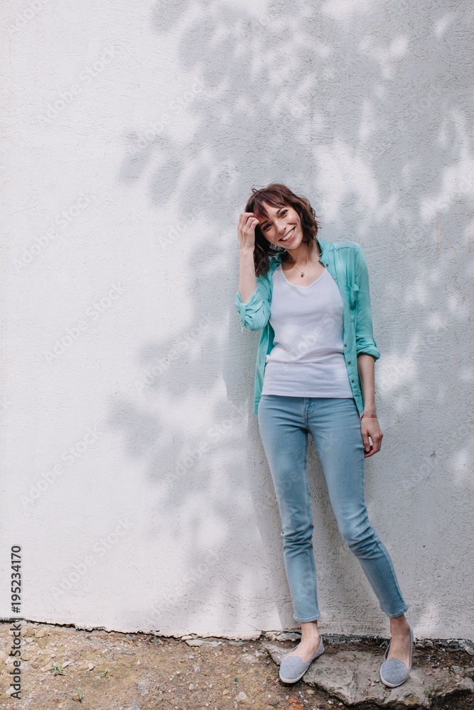 Smiling cute female stand in front of white wall with shadow of the tree Smiling cute female stand in front of white wall with shadow of the tree
