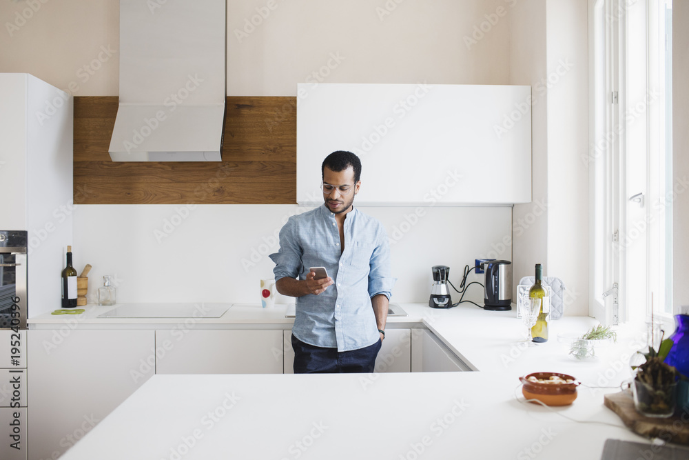 Young man texting on his cell phone in the kitchen Young man texting on his cell phone in the kitchen