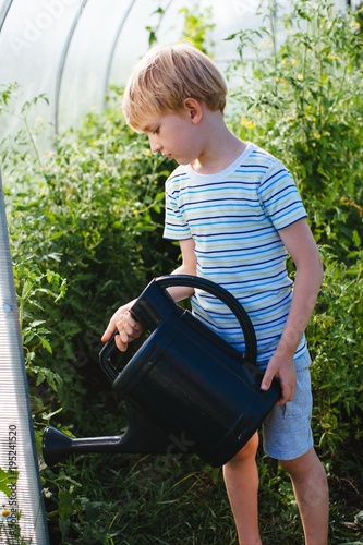 Cute blond boy watering the plants in greenhouse