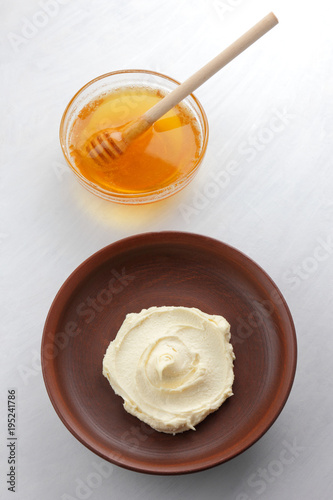 Sour cream, cottage cheese, dairy product in a clay bowl, cottage cheese on a white background in rustic style, honey and wooden stick, cream in a brown plate, French breakfast, copy space, minimalism