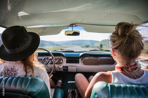 two women driving in a vintage car looking out at the open road