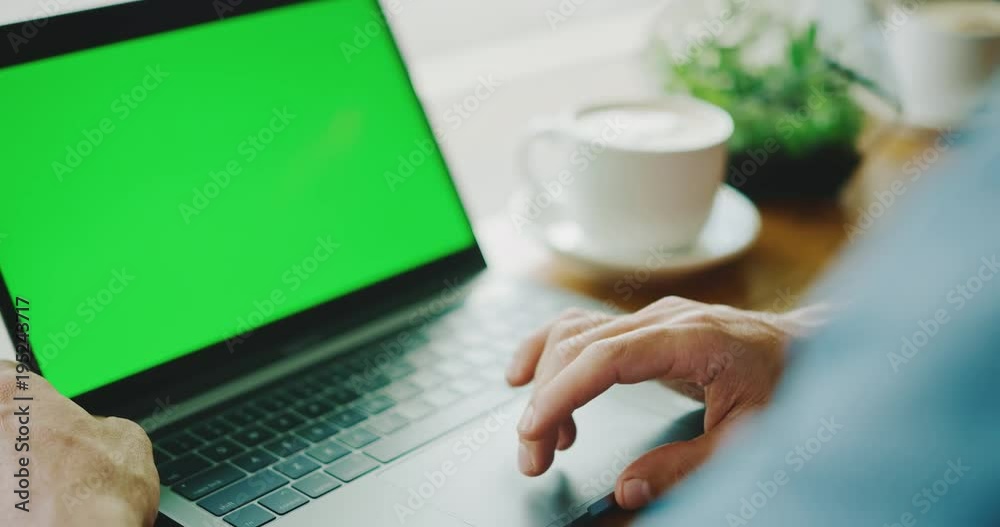Man working on laptop with green screen in coffee shop