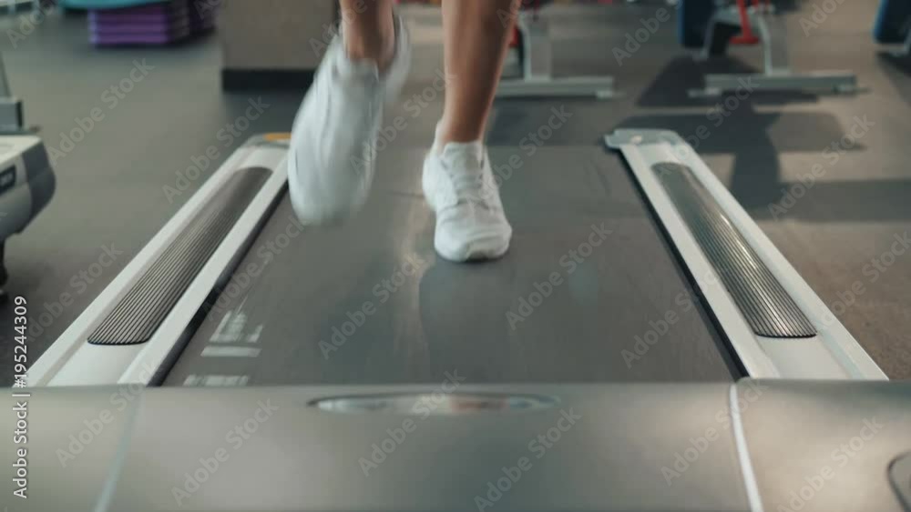 A close up of a woman running on a treadmill fast run. White sneakers shoes sport. Female runner training fast athlete A close up of a woman running on a treadmill fast run. White sneakers shoes sport. Female runner training fast athlete