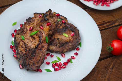 Steak on ribs, cooked on a grill with pomegranate on a white plate. Wooden rustic background. Top view