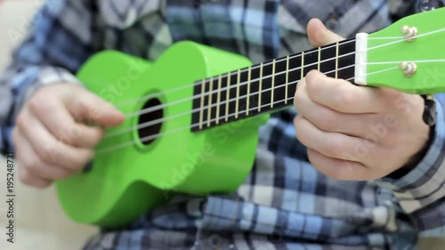 Portrait of a bearded hipster male in red hat playing on ukulele