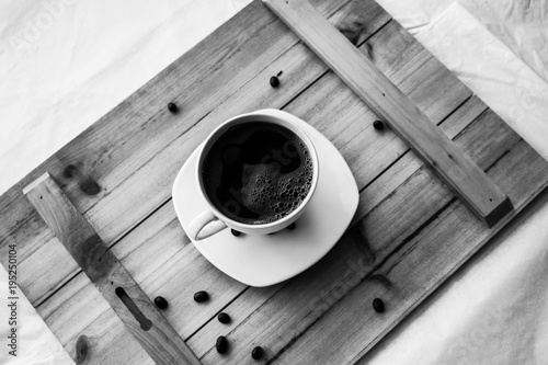 Single white cup with black coffee on wooden table with few beans black and white photography