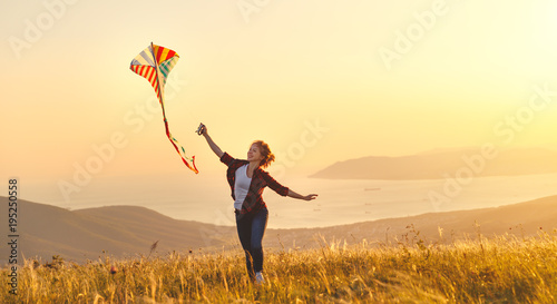 Tableau sur toile Happy young woman running with kite on glade at sunset in summer.