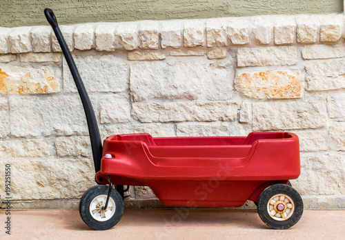 weathered red child's wagon against a sand colored limestone  block wall photo