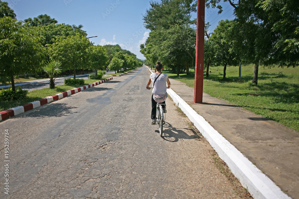 Obraz premium Lady cycles down a deserted road in Bagan, Burma