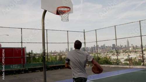 young man driving to basket - practicing his basketball game - scoring layup on outdoor court with view of Manhattan skyline New York City NYC in 4K and 1080 HD